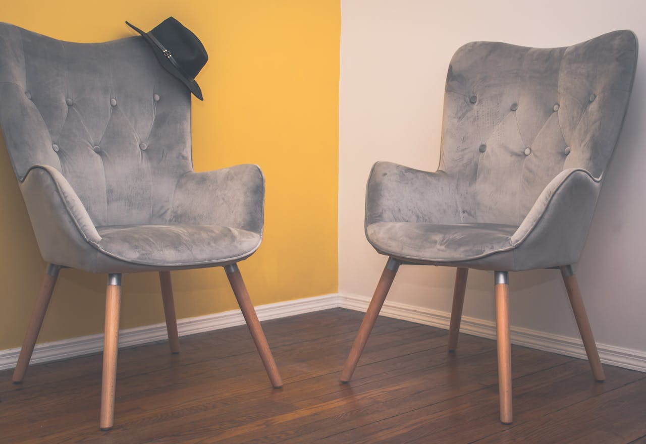Home Two contemporary gray armchairs in a minimalist interior with a yellow accent wall and wooden flooring.